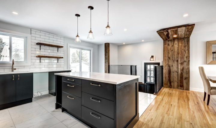 Newly remodeled kitchen with dark cabinetry and contrasting wooden beams, featuring a bright white island and subway tile backsplash.