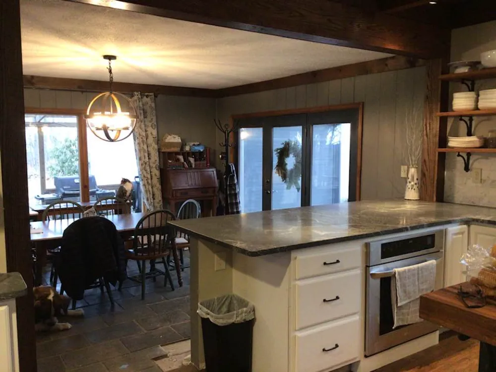 A view of a spacious room combining a kitchen and dining area, decorated with rustic furniture, a large dining table, and soft natural lighting.