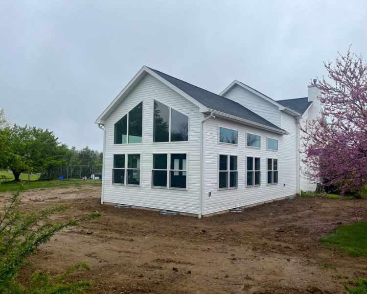 Contemporary style home addition with large windows and pristine white siding, set in a suburban environment with flowering trees.