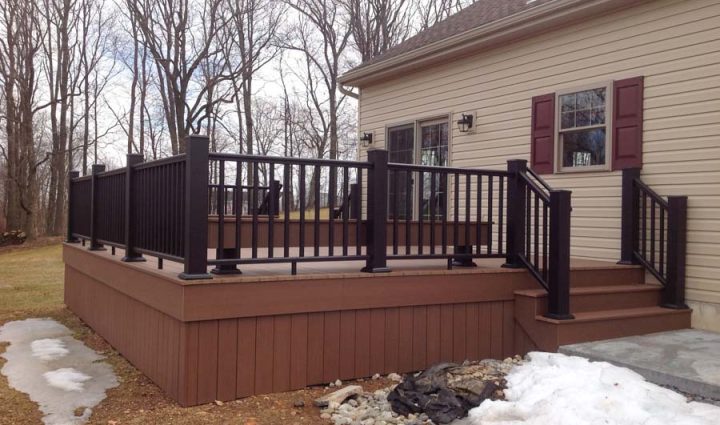 Modern outdoor deck featuring dark railing and steps, attached to a home with beige siding, providing a stylish space for outdoor relaxation.